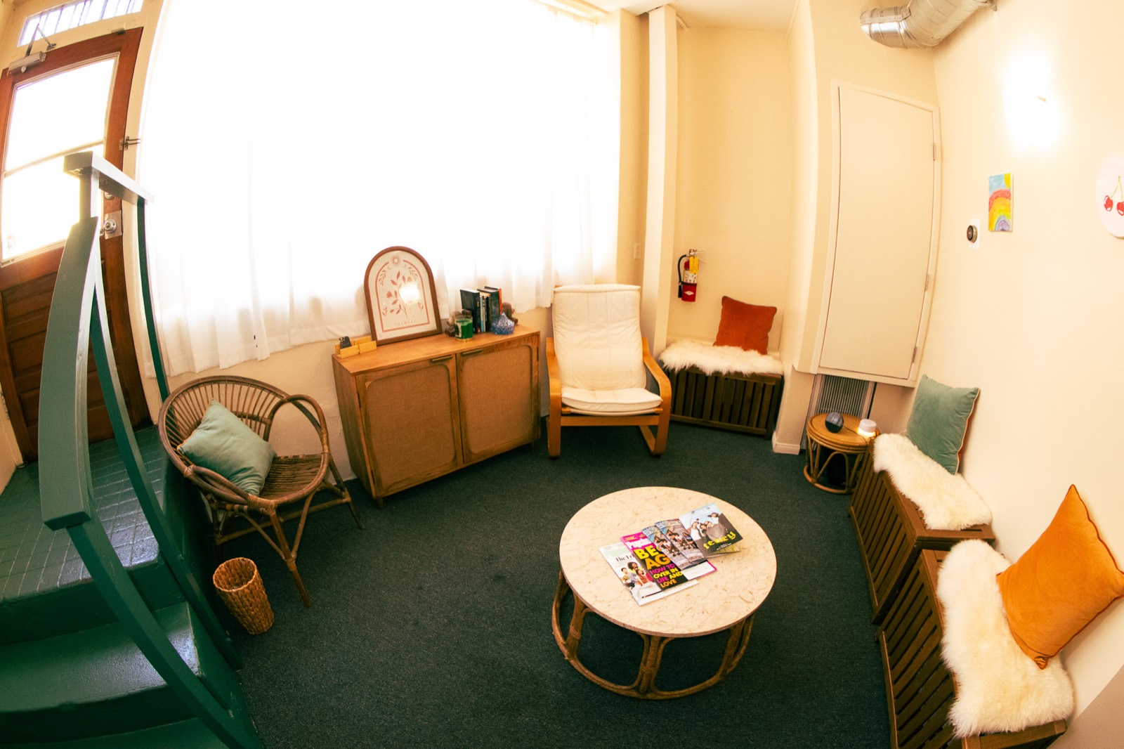 The waiting room: cream walls, a dark green staircase and stair rail, a wicker chair, a low round table with magazines on it, and bench seating with sheepskins and cushions.